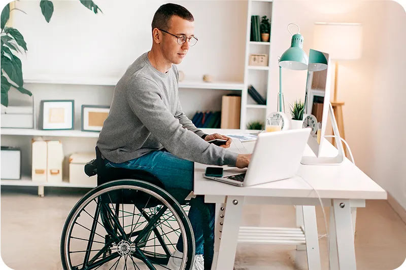 Un homme en fauteuil roulant travaille a son bureau dans un appartement Mobicap lumineux